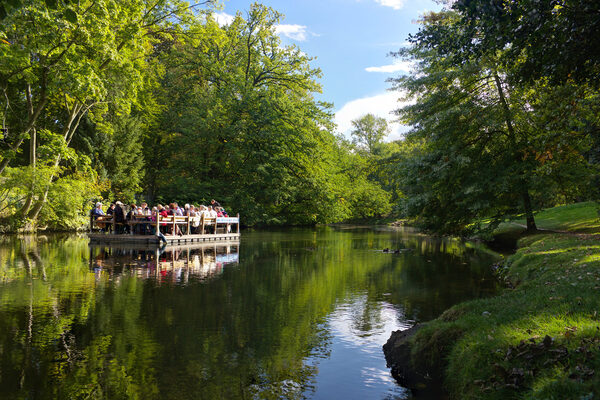 Ein großes Floß mit Personen, das auf einem Fluss fährt. (Wird bei Klick vergrößert)