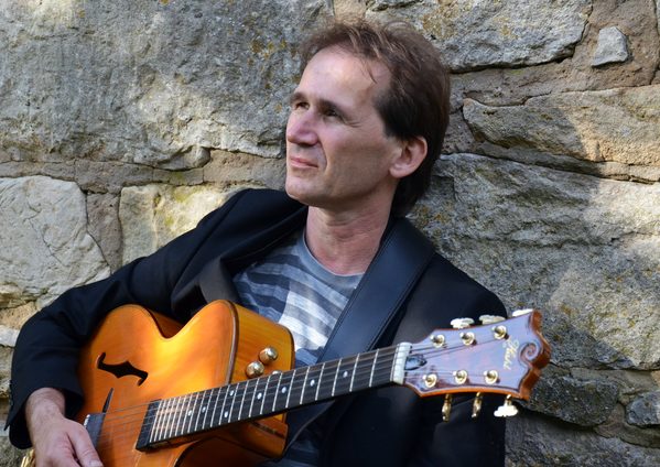Bild Dietmar Osterburg an einer Feldsteinmauer mit akustischer Gitarre