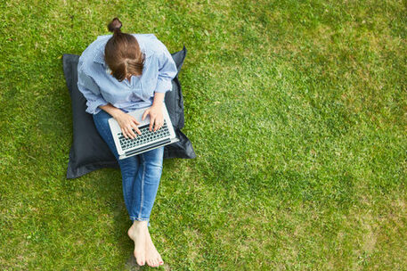 Woman as a freelancer on the laptop PC in the summer in the green garden on the meadow from above