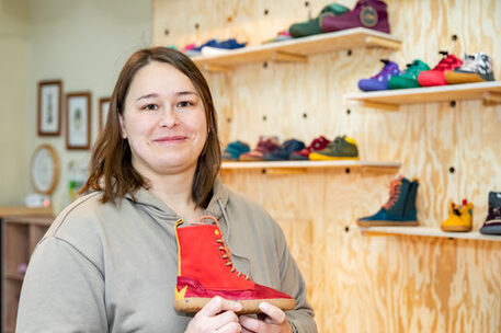 Das Bild zeigt die Inhaberin des Geschäfts "Wald Child" mit einem roten Barfußschuh in den Händen.