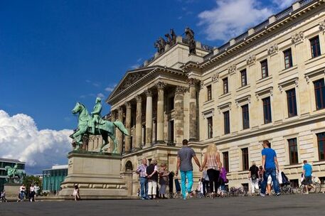 Das Bild zeigt den Eingang der schloss Arkaden Braunschweig mit Passanten. Links sind zwei Reiterstatuen zu sehen.