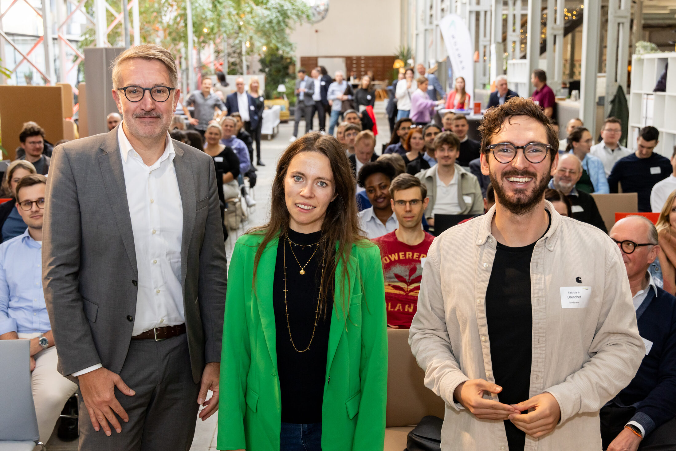 Das Bild zeigt drei Menschen vor einem Publikum. (Wird bei Klick vergrößert)