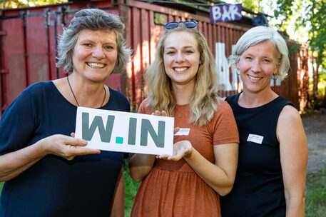 Das Bild zeigt drei Frauen, die ein Schild halten.