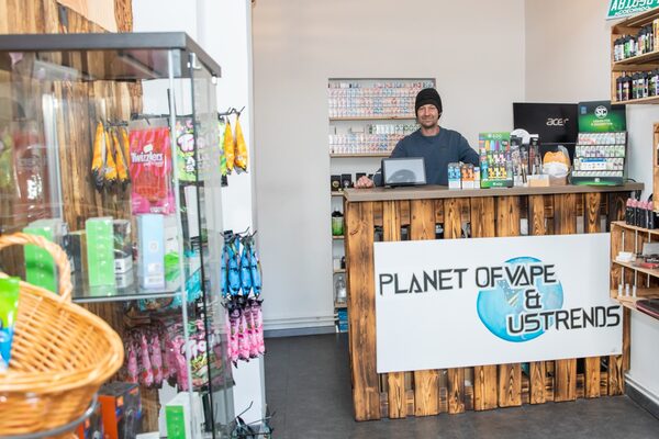 Das Bild zeigt den Inhaber des Geschäfts "Planet of Vape" hinter dem Verkaufstresen. (Wird bei Klick vergrößert)