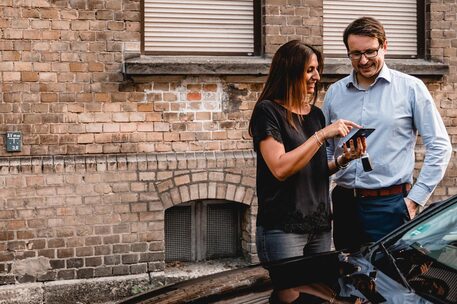 Eine Frau und ein Mann stehen mit einem Smartphone in der Hand am Auto