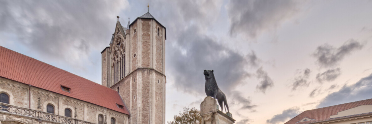 Das Bild zeigt den Braunschweiger Burglöwen in der Mitte und den Dom St. Blasii am linken Bildrand.