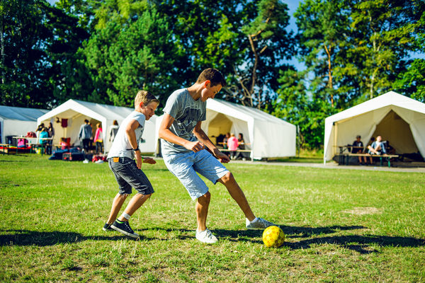 Jungen spielen Fußball auf Wiese vor Zelten