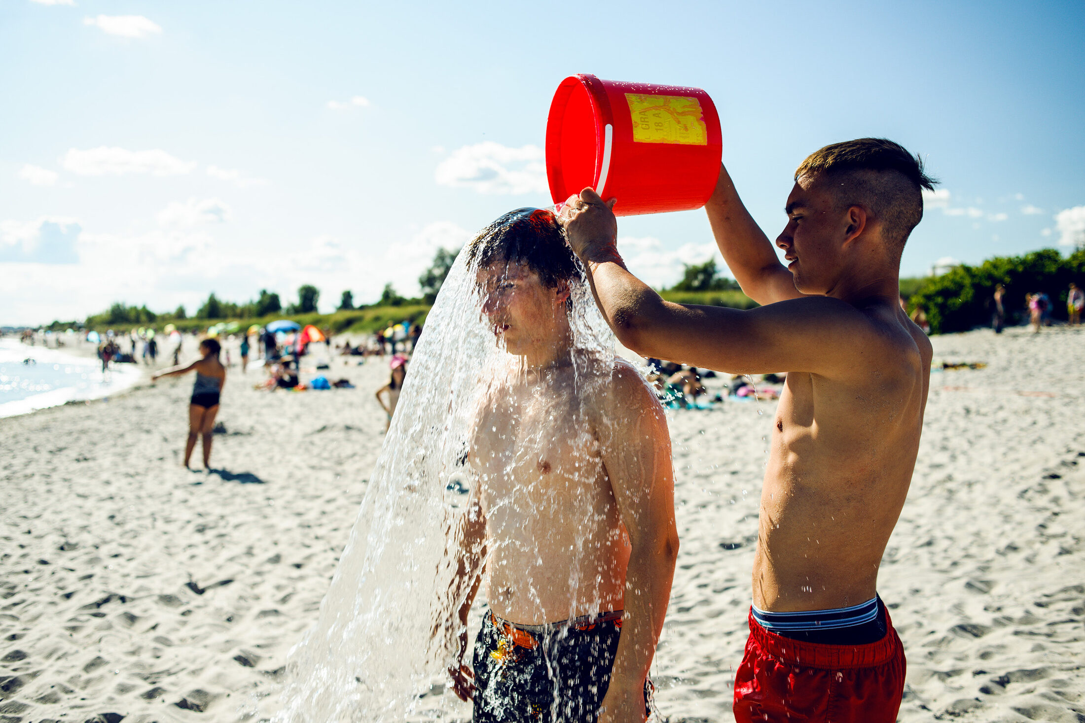 Junge kippt am Strand Wassereimer auf einen anderen (Wird bei Klick vergrößert)